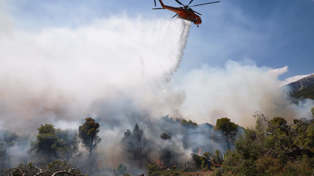 Dos helicópteros cisterna operando en el cielo de Grecia sobre una densa columna de humo provocada por los incendios forestales bajo fuertes vientos.
