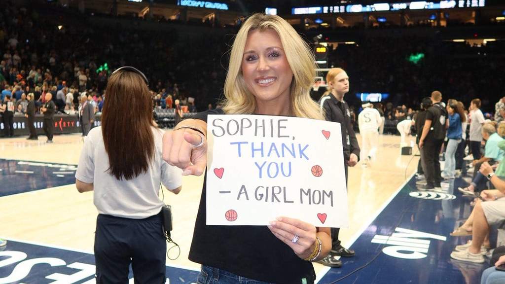 Riley Gaines sosteniendo el cartel de agradecimiento a la jugadora Sophie Cunningham en las gradas del estadio Target Center.